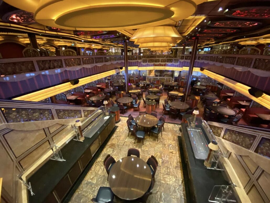 A spacious, elegantly decorated dining area aboard Carnival Freedom offers a variety of dining options. With multiple round tables and chairs, the room features a mirrored ceiling, gold and purple accents, and two levels with a central open view from the top floor, making it one of the finest places to eat.