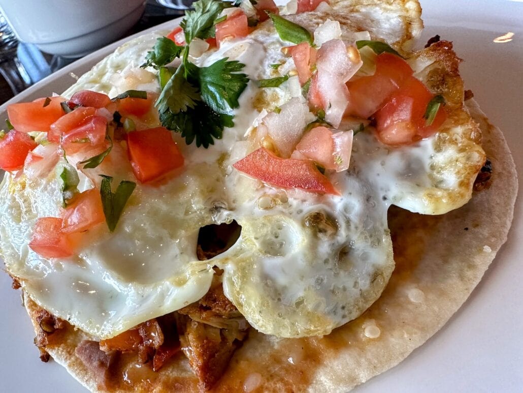 A plate with huevos rancheros tempts you on Carnival Freedom, featuring two sunny-side-up eggs on a tortilla with zesty salsa of diced tomatoes and cilantro, making it a must-try for travel dining enthusiasts seeking unique places to eat.