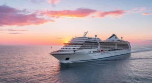 A large white cruise ship glides across a calm ocean under a colorful sunset sky with pink and orange clouds, offering the perfect backdrop for enjoying European cruise tips.