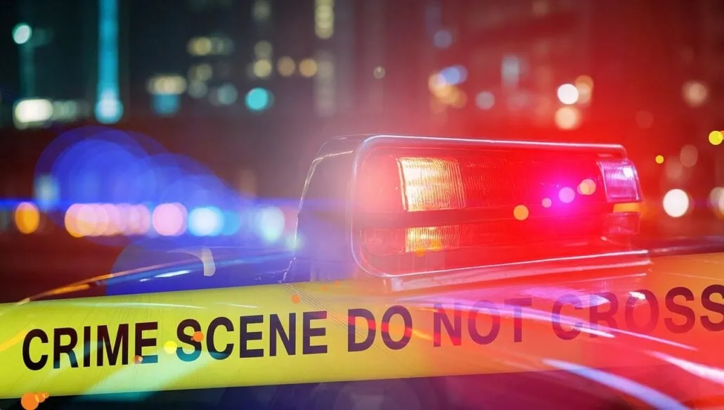A police car with flashing red lights is parked at a crime scene in downtown Charlottetown. Yellow tape reading "CRIME SCENE DO NOT CROSS" captures the gravity of a fatal accident, while the city lights blur hauntingly in the background.