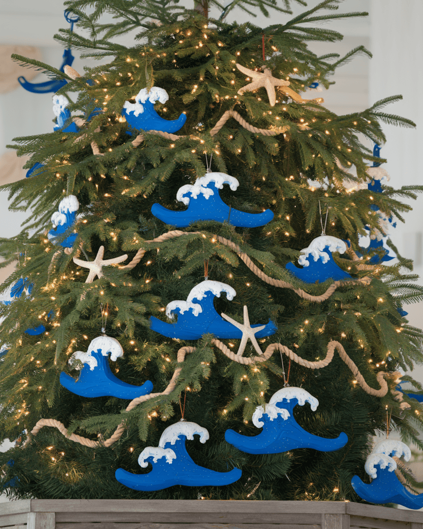 A Christmas tree adorned with blue and white wave-shaped ornaments, white starfish, and rope garlands brings a cruise-themed vibe to the holiday season. Lit with small white lights, it stands elegantly in a wooden box.