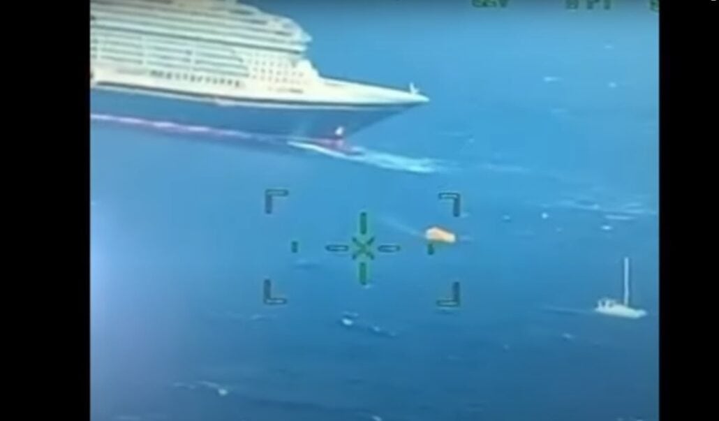 Aerial view of a large Disney ship sailing in the ocean. A smaller boat is visible nearby, alongside a small yellow object in the water, as if poised for rescues. The image appears captured through a device with targeting markers.