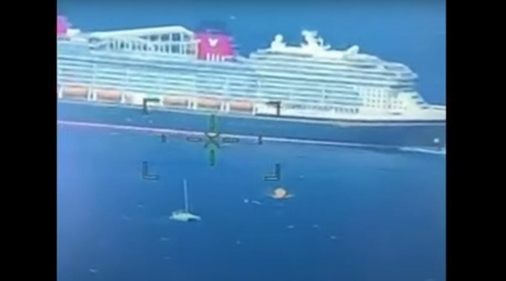 An aerial view captures a massive Disney ship cruising the calm ocean, with a smaller sailing vessel nearby. Crosshairs overlay the image, suggesting it's taken from a surveillance helicopter during a rescue mission. The sea is tranquil, and the sky is clear.