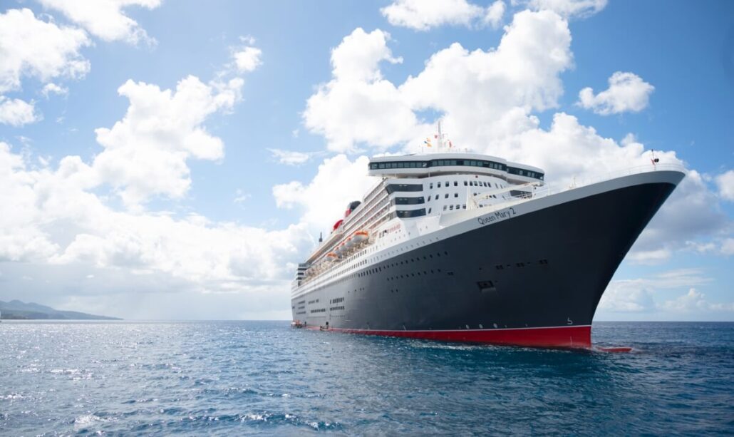 A large cruise ship with a dark hull and white upper decks is gracefully sailing in clear blue water under a partly cloudy sky. The ship's name stands out on the front, as if inviting passengers to explore the cognitive benefits of cruising. Land is visible in the distance on the left side.