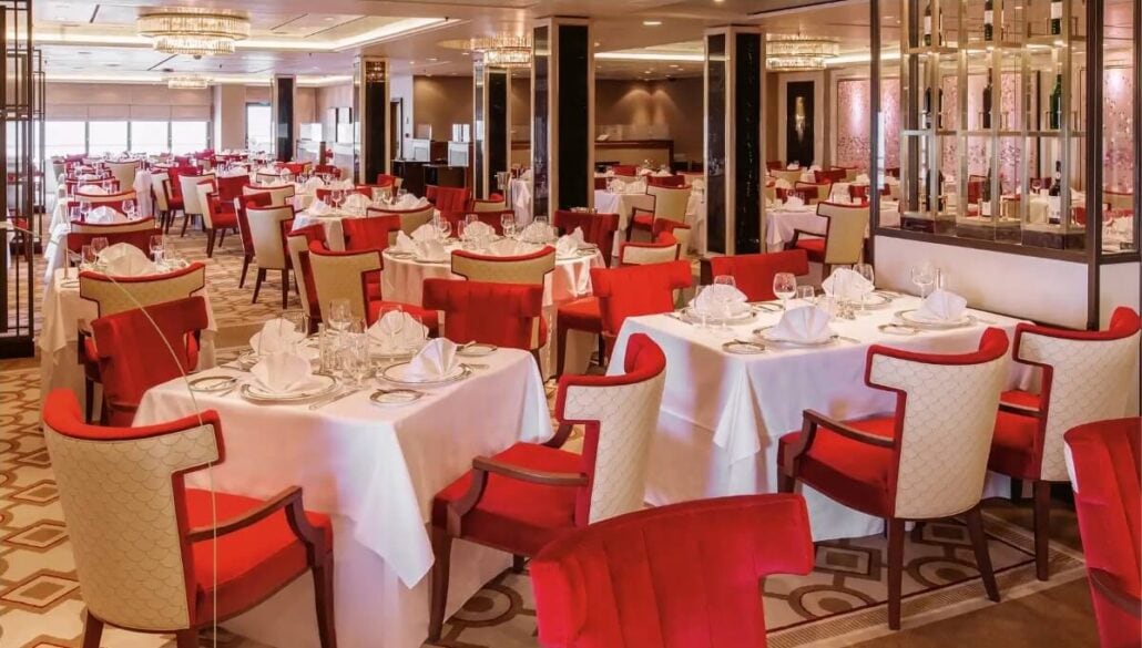 The spacious restaurant aboard the Queen Mary 2 features red and beige upholstered chairs around square tables with white tablecloths. Elegantly lit by chandeliers, the decor is modern and sophisticated, offering a serene dining experience after recent concerns of a gastro outbreak.