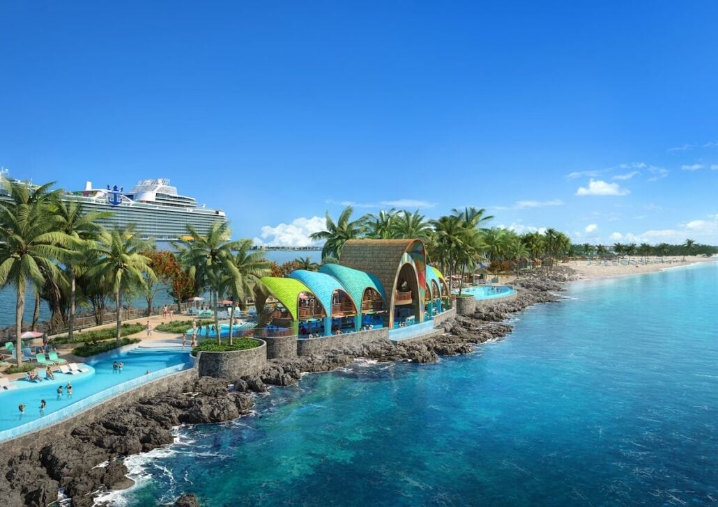 A tropical beach scene with a Royal Caribbean cruise ship docked near Nassau, Bahamas, showcases a vibrant coastal resort with colorful roofs. The foreground displays rocky shorelines and turquoise waters, with palm trees lining the area and the Royal Beach Club's sandy beach extending into the background.
