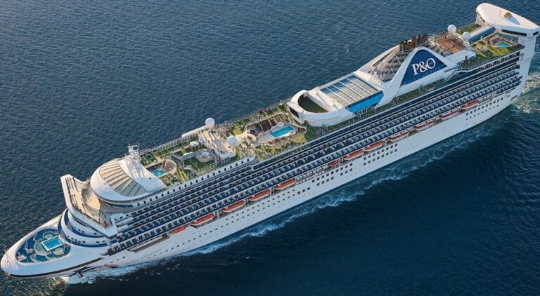 Aerial view of a large white cruise ship, brandishing a P&O logo on its funnel. With multiple decks featuring amenities, including two blue swimming pools, this P&O Australia vessel offers both encounter and adventure as it sails on the calm ocean.