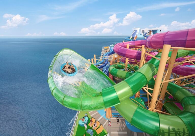 A group of people ride a green water slide aboard Royal Caribbean's Star of the Seas. The slide features a translucent section extending over the deck, offering stunning ocean views. Various other colorful slides and the open sea are visible in the background under a blue sky, highlighting the excitement of new sailings.
