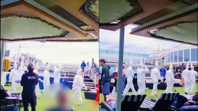 People in hazmat suits are walking in a line on a cruise ship deck, a curious sight amidst an unexpected mishap. Some passengers are observing, dressed casually, with some seated on lounge chairs. The sky is overcast, adding to the peculiar atmosphere aboard the cruise line.