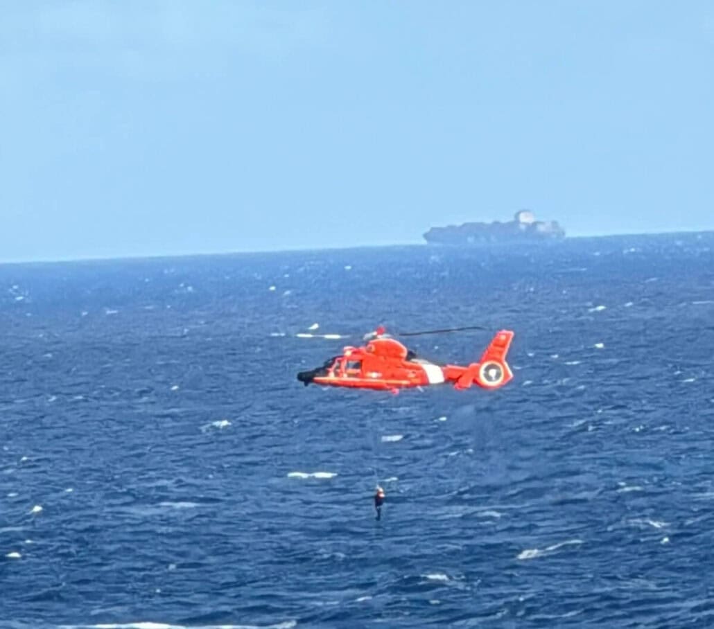 A red and white helicopter hovers over the ocean in a daring rescue. Below, a person is being lifted from the water while a Royal Caribbean cruise ship glides on the horizon under a clear sky.