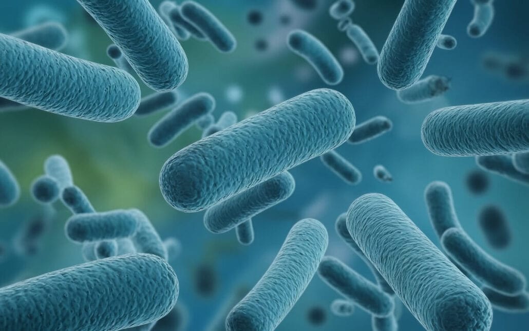 Illustration of blue, rod-shaped bacteria linked to Legionnaires’ Disease floating in a blurred, green and blue background, suggesting a microscopic view. The bacteria have a textured surface and vary slightly in size and orientation.