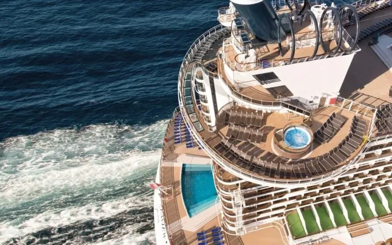 Aerial view of a Brazilian cruise ship's top deck featuring a swimming pool and a circular hot tub. Rows of lounge chairs are neatly arranged around the pool area as the ship sails on a calm blue sea.