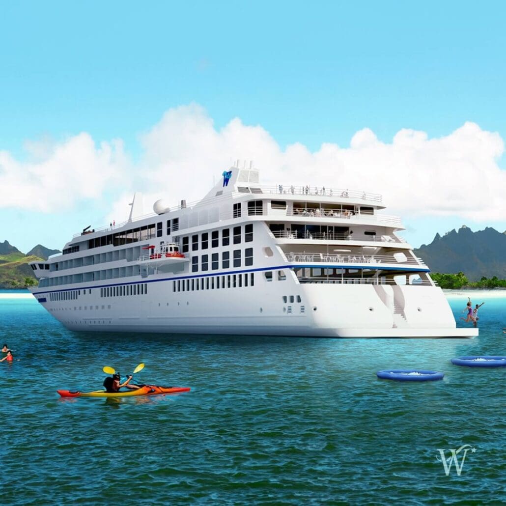 A large white cruise ship from the New Ships 2025 fleet is anchored in a calm turquoise sea under a clear blue sky. People are kayaking nearby, and others are on floating platforms. In the background, lush green mountains complete this serene scene.
