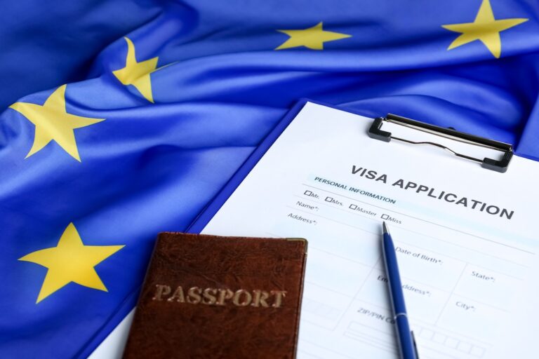 A visa application form rests on a clipboard next to a dark brown passport and a pen, as UK travelers prepare for increased ETA Visa fees. The background displays the European Union flag with yellow stars on a blue field.