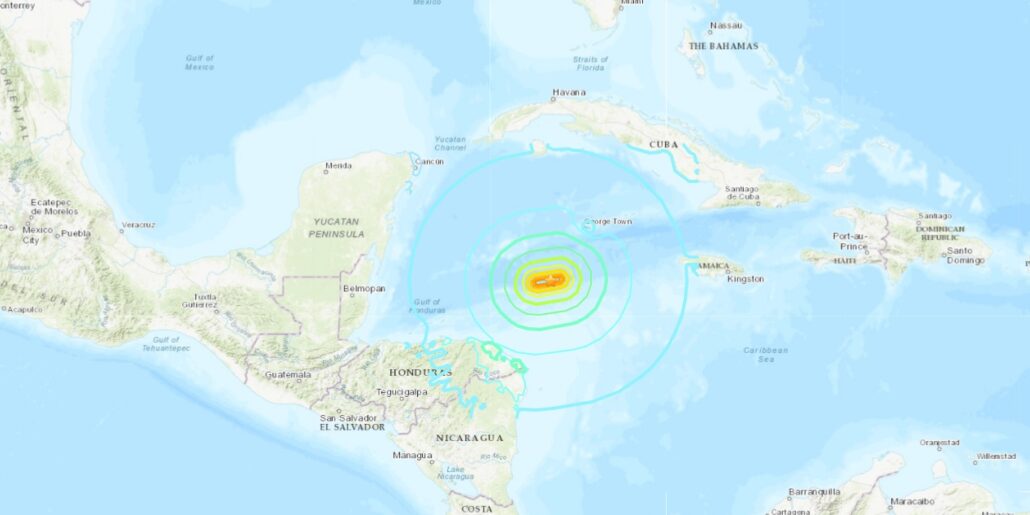 A map of the Caribbean region shows a seismic activity area. Concentric colored lines illustrate intensity zones, with the epicenter near the Cayman Islands in the Caribbean Sea. Nearby lies a cruise route, where ships like Disney Treasure sail past Cuba, Jamaica, and Honduras.