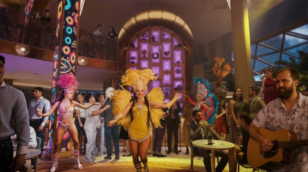 Dancers in colorful costumes captivate the lively crowd at The Bazaar nightclub, where vibrant lighting and decor set the scene. Musicians play on the right, adding to the festive atmosphere of this destination-focused cruising hotspot.
