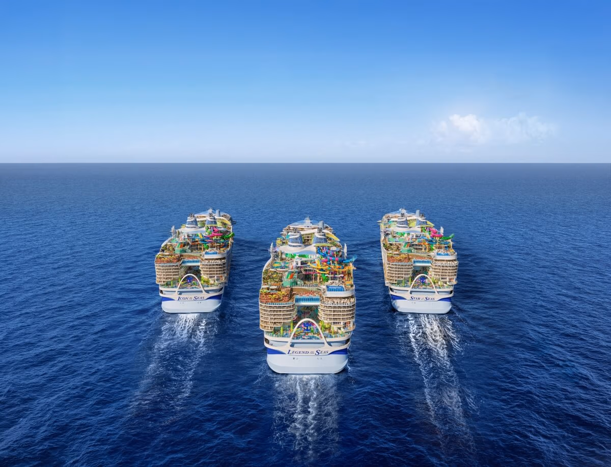 Four Icon-Class ships sail side by side on a calm ocean under a clear blue sky. Each Royal Caribbean ship features multiple decks with various structures and decorations, as they move forward leaving trails in the water.