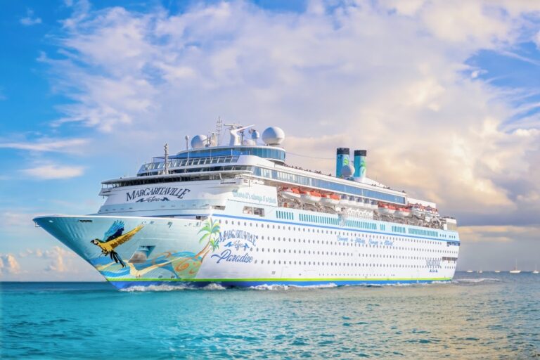 A large white cruise ship, adorned with tropical designs and the name "Margaritaville at Sea Paradise" on its side, sails on a calm ocean under a partly cloudy sky, embodying a transformation into an island dream.