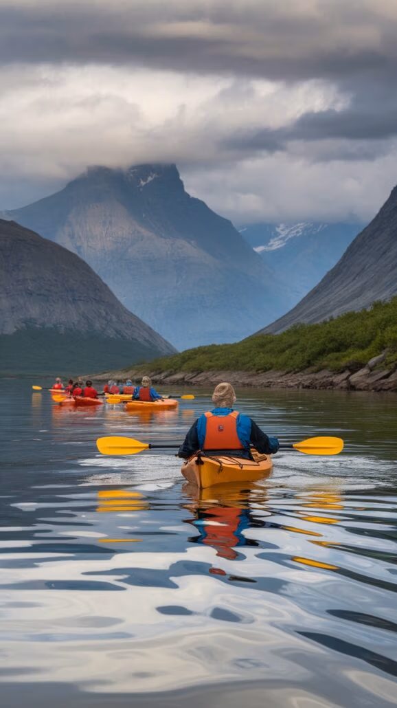 A group of adventurers kayaking on a calm Alaskan river, surrounded by towering mountains under a cloudy sky. The lead kayaker, in an orange kayak with a blue jacket and orange life vest, guides the team. Lush green vegetation lines the riverbank. Essential tips for this journey: embrace the majestic views!.
