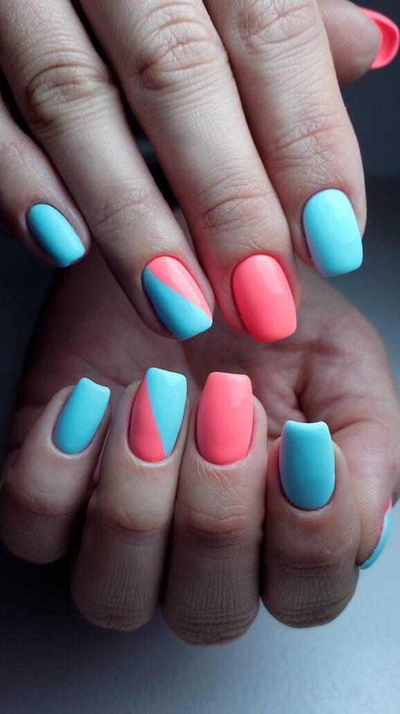 Close-up of hands showcasing Cruise Nails, featuring manicured nails in alternating shades of blue and coral. The ring fingers boast a diagonal split design with both colors. Short and shiny, these stylish ideas are set against a smooth, neutral gray backdrop.