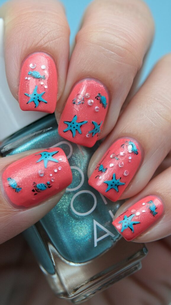 A hand with coral pink nails adorned with turquoise starfish and tiny white dots captures the essence of the best cruise nails. In the background, a teal polish bottle peeks through, reminiscent of a serene trip to the Bahamas.