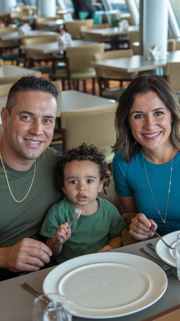 A family of three sits at a restaurant table, perhaps planning their next cruise adventure. A man is on the left, a woman on the right, and a young child in the middle holding a fork. They are all smiling, surrounded by empty plates and cutlery. The background shows other dining tables buzzing with excitement.