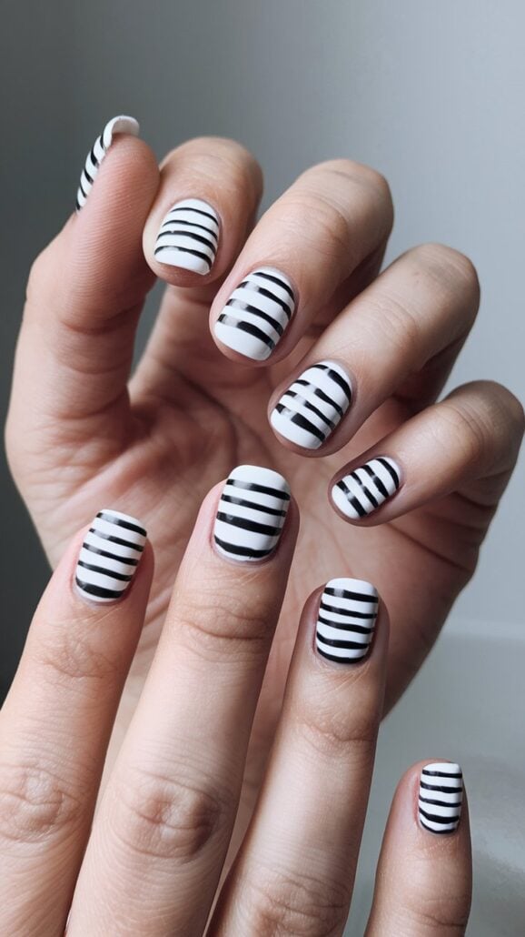 Hands with black and white horizontally striped nail art exude stylish ideas. The nails, medium in length, boast a glossy finish, set against a soft, neutral background. Perfect for those seeking cruise nails that make a subtle yet elegant statement.