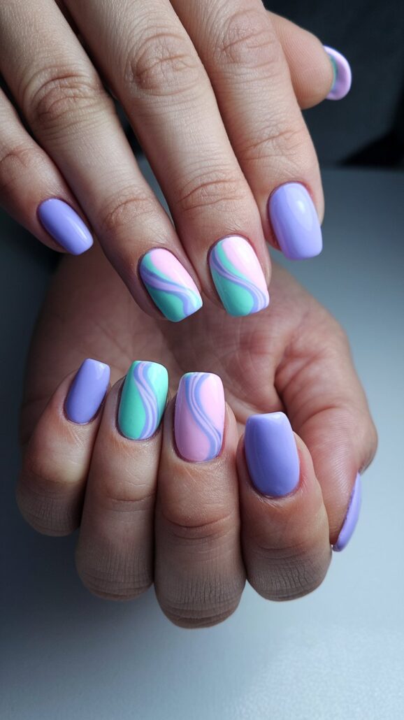 Close-up of hands with manicured nails, offering stylish ideas for your next look. The pastel colors feature a mix of solid lavender and a swirl pattern in pink, green, and light blue. These adore-worthy nails are shaped in a chic medium square style, perfectly capturing the essence of cruise nails.