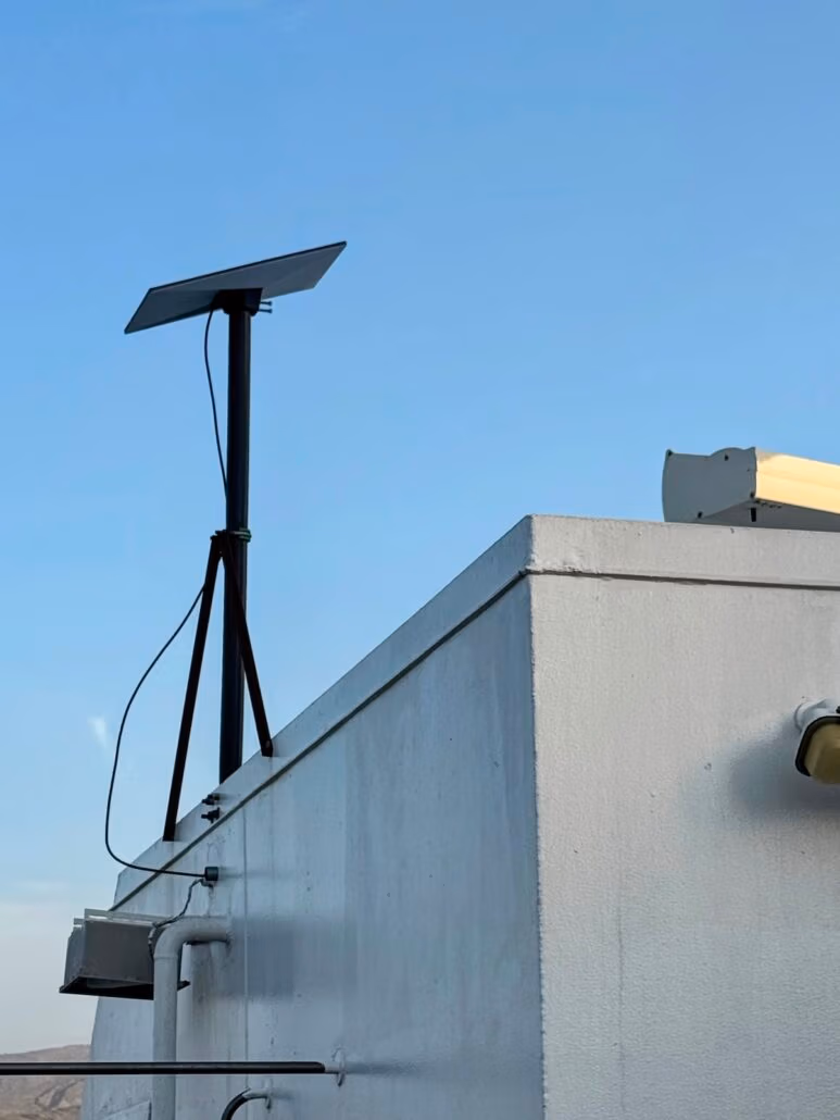A satellite dish is mounted on a tripod atop a white, flat-roofed building under a clear blue sky, much like one might spot on a Celestyal Journey. Cables snake down the side of the structure, hinting at adventures beyond the typical cruise or mundane destinations.