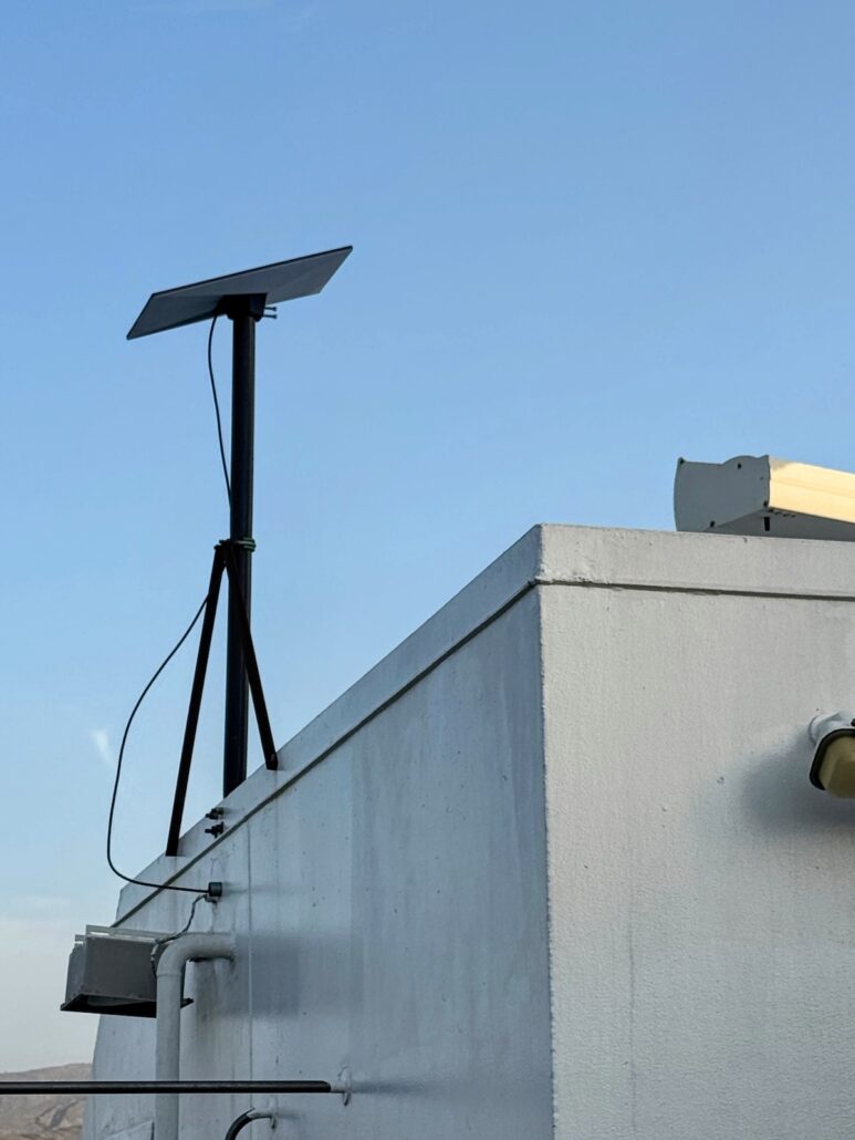 A satellite dish is mounted on a tripod atop a white, flat-roofed building under a clear blue sky, much like one might spot on a Celestyal Journey. Cables snake down the side of the structure, hinting at adventures beyond the typical cruise or mundane destinations.
