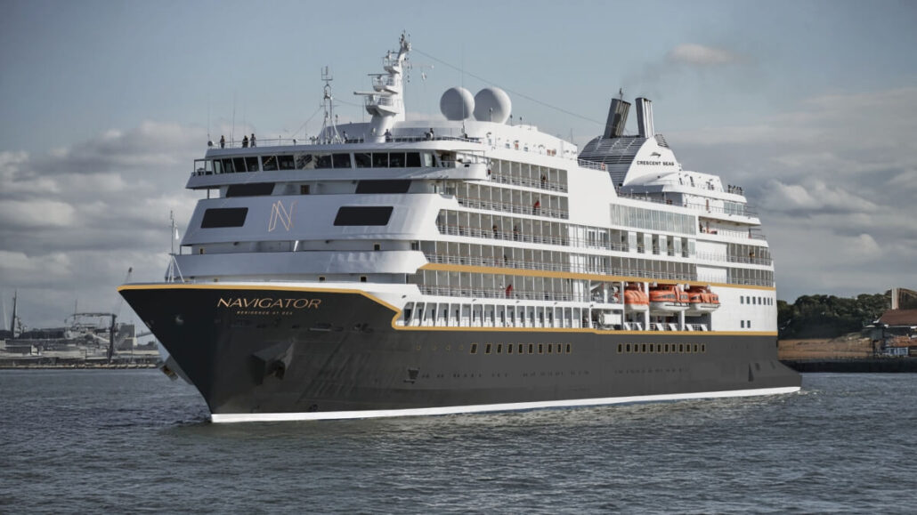 The elegant black and white cruise vessel, "Navigator," glides across the water with grace. As a splendid representative of the Regent Seven Seas fleet, it flaunts multiple decks and visible lifeboats. The sky is partly cloudy, with land appearing in the background.