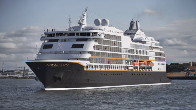 The elegant black and white cruise vessel, "Navigator," glides across the water with grace. As a splendid representative of the Regent Seven Seas fleet, it flaunts multiple decks and visible lifeboats. The sky is partly cloudy, with land appearing in the background.