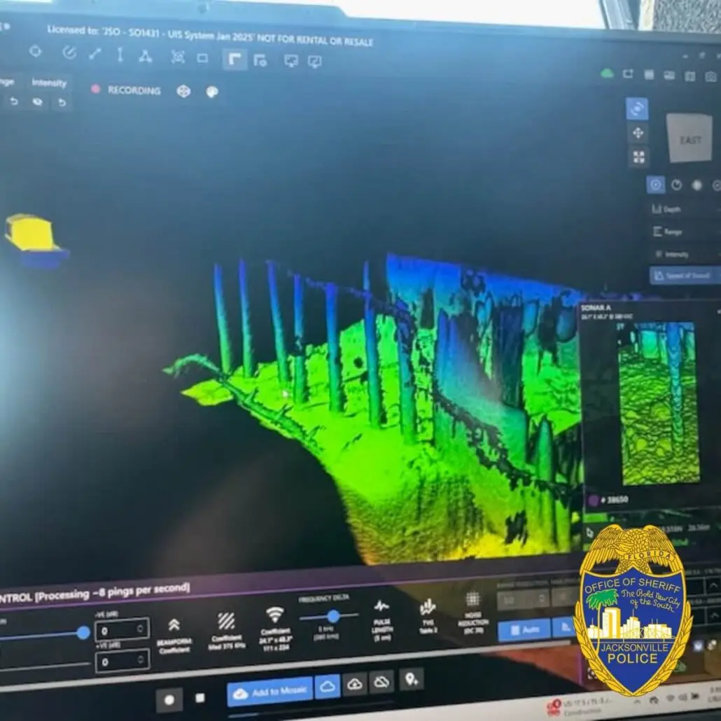 A computer screen displays a 3D lidar scan of a color-coded terrain and urban structures, alongside the Office of the Sheriff Jacksonville Police badge. In the corner, a Carnival Cruise Ship's route for its Jacksonville arrival is highlighted, hinting at a coordinated Coast Guard search and rescue drill.