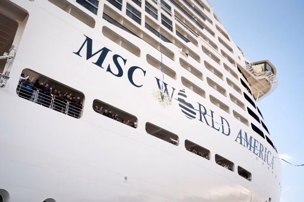 The image captures the side of a large cruise ship, "MSC WORLD AMERICA," with a festive crowd seen through the windows and on a lower deck. A bottle hangs suspended in mid-air, hinting at a triple celebration involving its sister vessels.