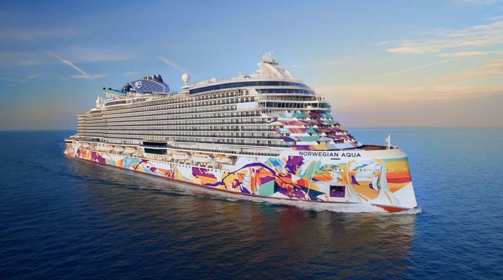 The grand cruise ship "Norwegian Aqua," adorned with Prima Plus artwork, glides gracefully on calm ocean waters. Its vibrant hull reflects the twilight hues as the sky embraces a few scattered clouds at sunset.