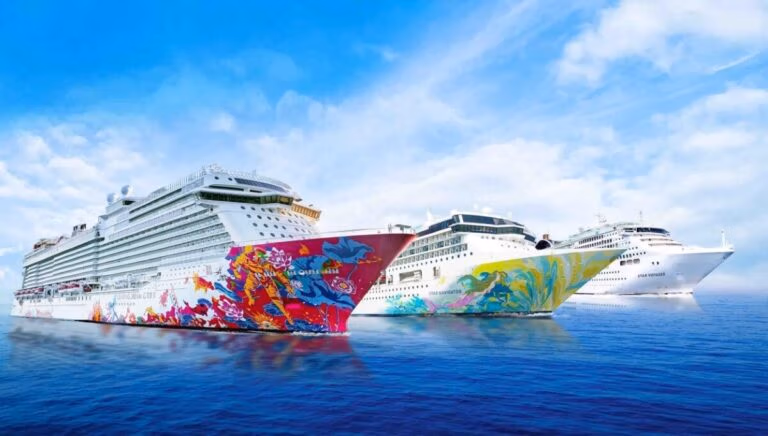 Three large, colorful cruise ships from Dream Cruises are sailing on a calm sea under a blue sky with scattered clouds. The ships feature vibrant artwork on their hulls and are moving in the same direction.
