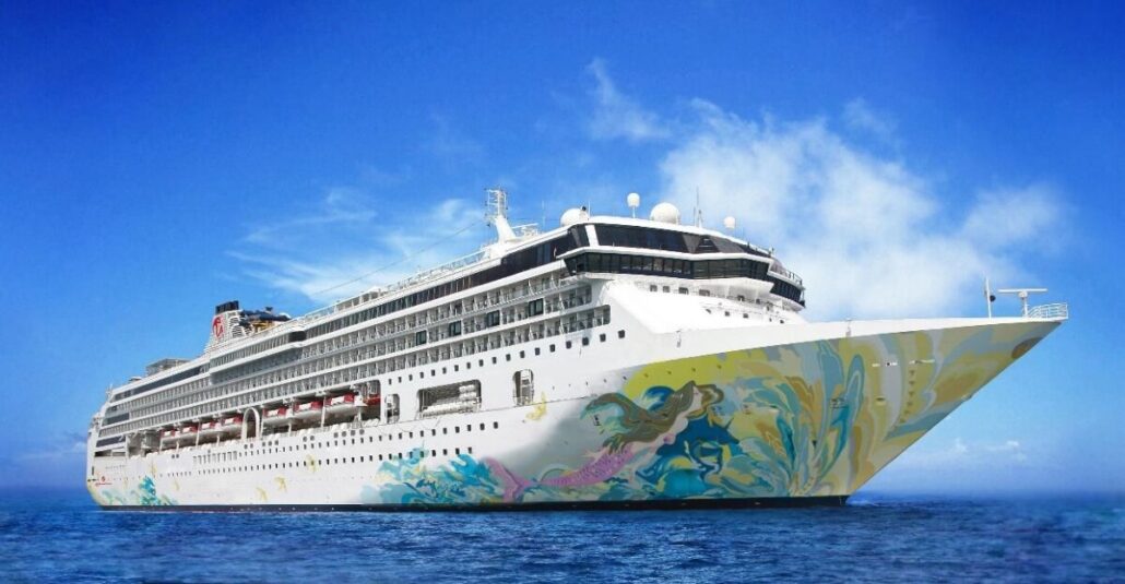 A large white cruise ship with colorful artwork on the bow, part of the luxurious Resorts World Cruises fleet, sails through calm blue waters under a clear sky. The ship features multiple decks and windows, with antennas and other equipment visible on the top deck.