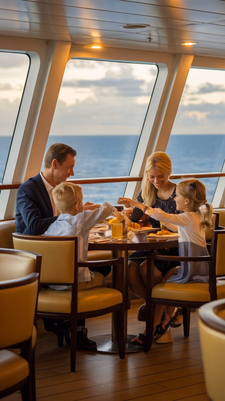 A family of four enjoys a meal on their dream vacation aboard a Caribbean cruise. Through large windows, the ocean glimmers, adding magic to their shared moments. The parents smile while the children excitedly reach for the food, perfectly capturing the essence of unforgettable family travel.