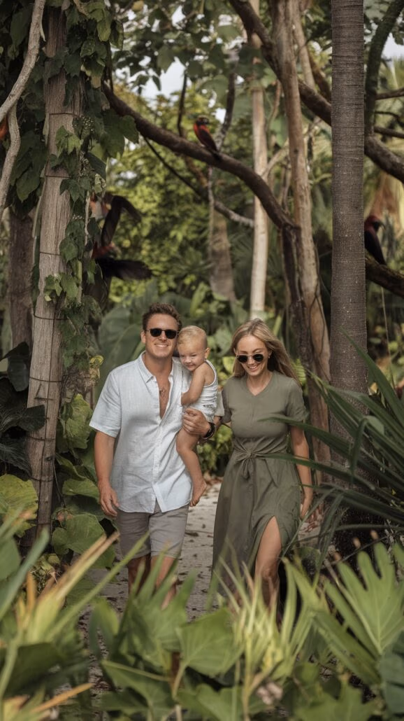 A couple strolls outdoors with their young child, embodying family bonding activities amid lush tropical vegetation. The man in a light shirt and shorts cradles the child on his hip, while the woman, in a green dress, enjoys the serene setting reminiscent of a Caribbean cruise's natural beauty.