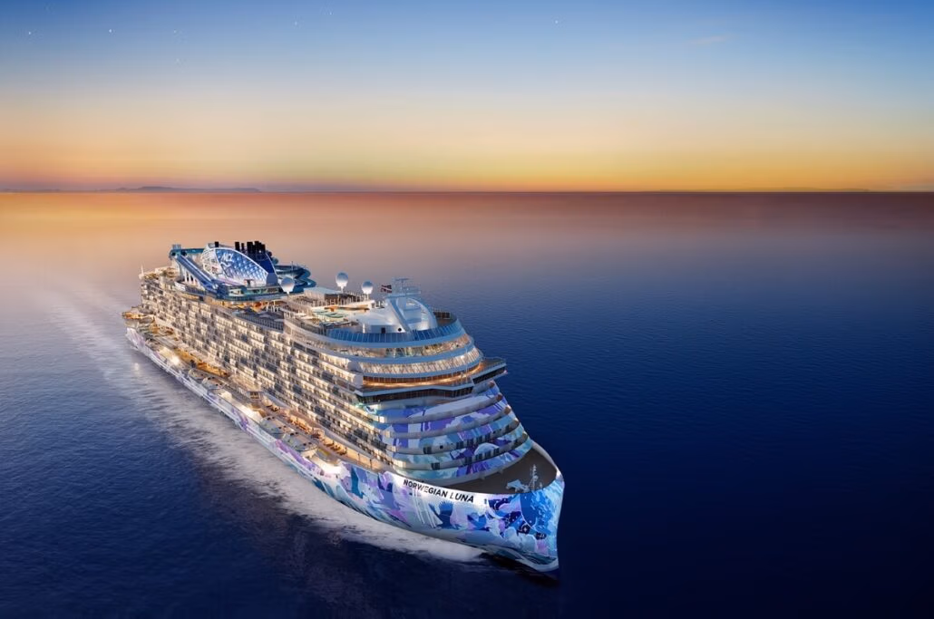 The Norwegian Luna, a large, modern cruise ship, gracefully sails on calm waters at sunset. Newly introduced at its 2026 launch, the vessel boasts intricate exterior designs. The sky unfolds in a gradient of orange and blue hues with stars starting to appear.