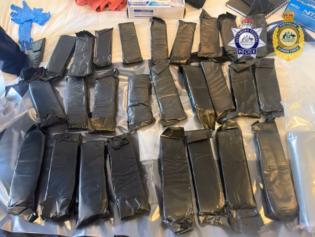 Several rectangular packages wrapped in black material are laid out on a surface, part of a major cocaine bust. Logos of the Australian Federal Police and Australian Border Force are visible in the top right corner, marking a significant operation that could lead to multiple life sentences.