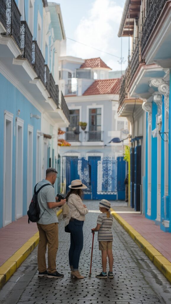 A family of three strolls down a narrow cobblestone street lined with pastel-colored buildings and balconies, soaking up the Caribbean sun. The adults consult a smartphone while the child cheerfully wields a red walking stick, capturing moments from their cruise adventure.