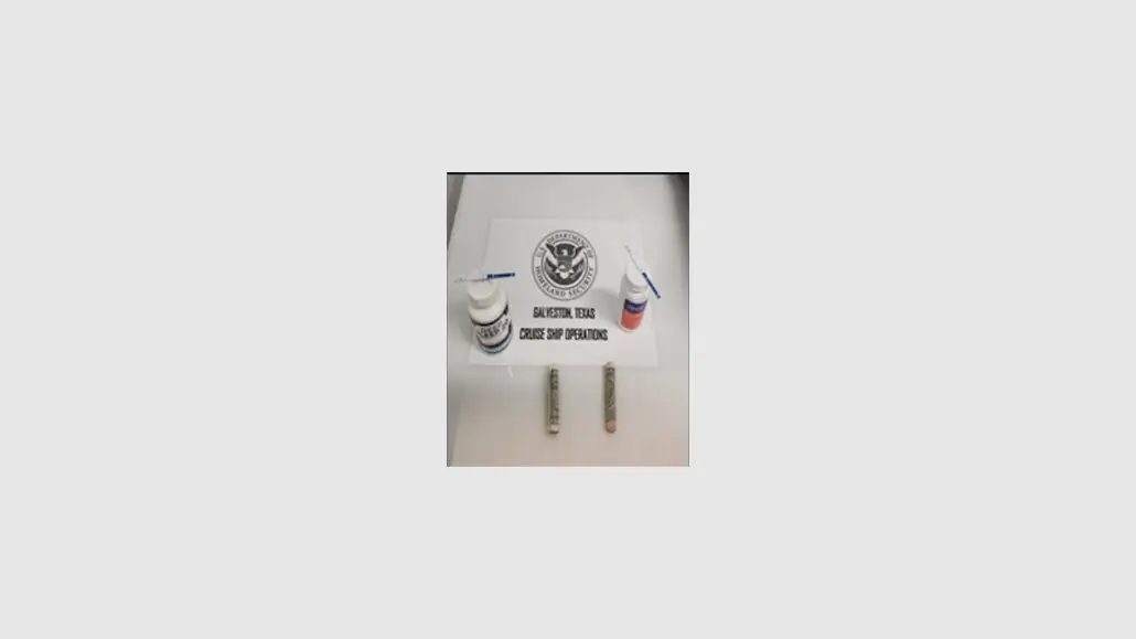 A table displays a sign with the U.S. Department of Homeland Security seal, two bottles labeled as drug test products, testing swabs, and two rolled paper items—possibly currency—from a Galveston cruise passenger arrest for drugs in luggage.