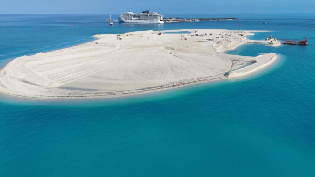 Aerial view of a private island under construction in turquoise water, with construction vehicles visible and an MSC Cruises ship docked at a distant pier.
