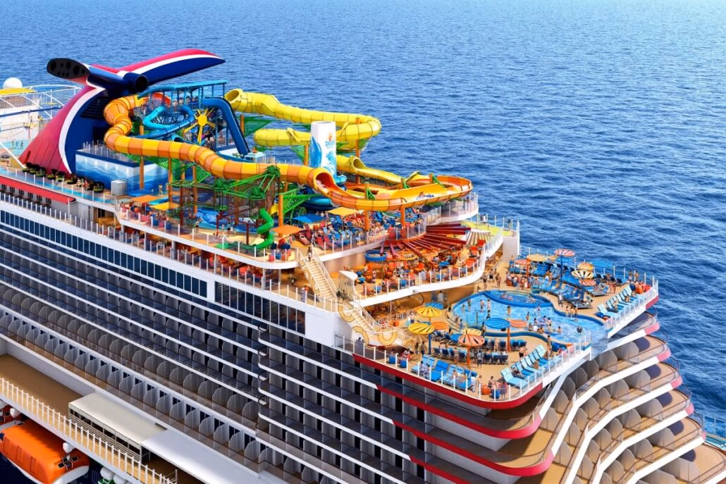 A large Carnival cruise ship features a colorful sprawling water park on its upper deck, complete with multiple slides, pools, and sunbathing areas. As it glides across the calm blue sea under a clear sky, guests can enjoy VIFP program perks for an unforgettable experience.