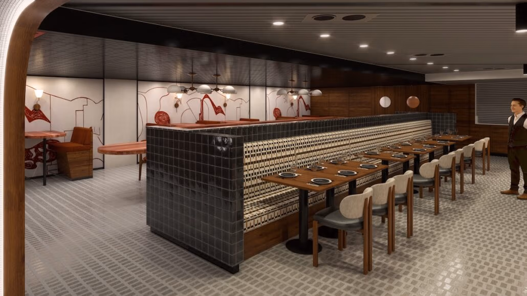 A modern Spanish tapas bar interior features a long bench with black and white patterned upholstery. Tables are set with plates and cutlery. Booths with red accents line the opposite wall, reminiscent of Virgin Voyages' Brilliant Lady decor. Ceiling lights provide ample illumination.