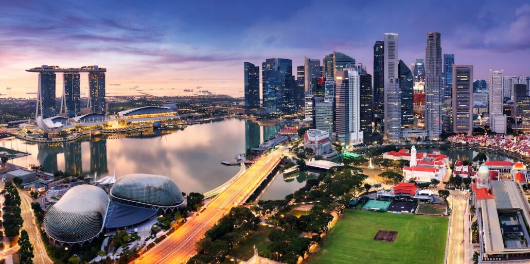A panoramic view of Singapore’s Marina Bay at dusk, featuring skyscrapers, the Marina Bay Sands hotel, the Esplanade Theatres, and busy roads with light trails along the waterfront.