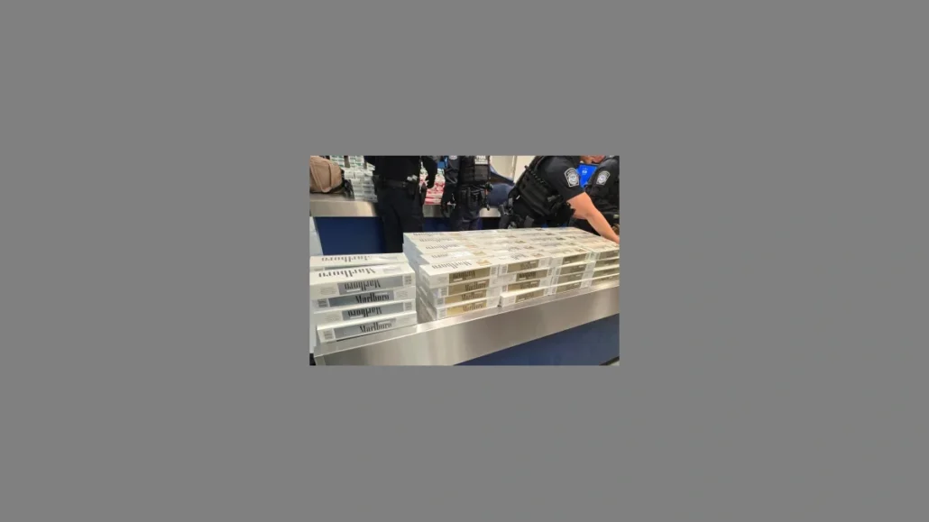 Several stacks of contraband cigarettes are displayed on a counter, with uniformed CBP officers standing behind them. Only the torsos and arms of the officers, who intercepted the items possibly from cruise guests, are visible.