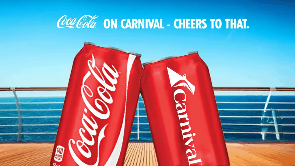 Two red soda cans, one with the Coca-Cola logo and one with the Carnival logo, are touching in front of a cruise ship railing on Carnival Ships, with the ocean and blue sky in the background. Text above reads, "On Carnival - Cheers to That.