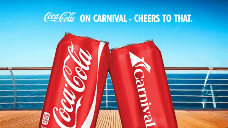 Two red soda cans, one with the Coca-Cola logo and one with the Carnival logo, are touching in front of a cruise ship railing on Carnival Ships, with the ocean and blue sky in the background. Text above reads, "On Carnival - Cheers to That.